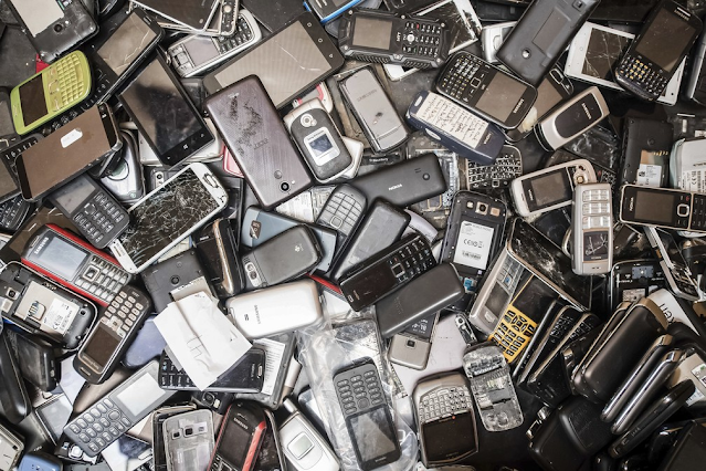 A imagem mostra vários celulares antigos e novos, descartados em um lixão.